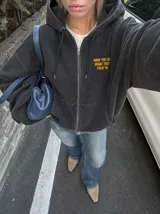 Hoodie canguro con cierre frontal, color negro con efecto acid wash, con capucha y bolsillos tipo canguro. Presenta el texto estampado en amarillo "Now You Do What They Told Ya" en el pecho.