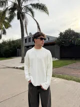 Sweater de punto color blanco con diseño asimétrico, presentando una mitad lisa y la otra mitad con tejido de ochos. Posee cuello redondo, mangas largas y un calce relajado.