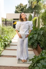 Blusa blanca de algodón con mangas al codo y puños elásticos, con tres volados en las mangas y cierre con botón en la espalda.