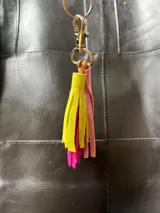 Llavero con borlas de gamuza multicolor, compuesto por un aro metálico con cierre de mosquetón y una placa metálica grabada con la marca Sierra Mora.