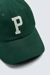 Gorra de seis paneles confeccionada en tejido de algodón, color verde oscuro, con parche frontal de letra P en color crema y ajuste posterior.