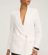 Blazer blanco de corte sastre, cruzado con doble botonadura de dos botones color beige. Presenta solapas de muesca y bolsillos de ojal con tapa en la parte delantera.