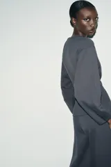 Jersey de cuello redondo y manga larga, confeccionado en tejido de punto elástico con trama compacta. Presenta un diseño con pinzas en la cintura que le otorgan una silueta entallada.