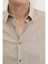 Camisa de vestir color beige claro, corte slim, de popelín de algodón elástico, con cierre frontal de botones y logo CK bordado en el pecho.