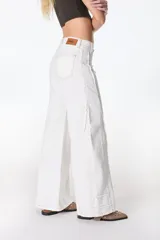 Jean color beige de corte recto, con detalles de costuras deshilachadas en los laterales y etiqueta de cuero marrón con el logo "PETRA" en la parte trasera de la cintura.