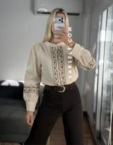 Camisa de manga larga color blanco con bordados geométricos en negro a lo largo de la botonadura frontal y en los puños. Presenta cuello mao y cierre frontal con botones.