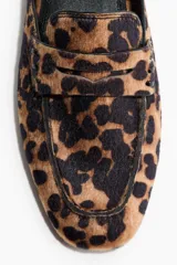 Mules estilo mocasín con punta redonda, modelo penny con costura tradicional en el empeine, forro interior negro y exterior con estampado animal print de leopardo.
