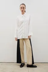 Pantalón de corte recto y tiro alto, confeccionado en algodón con diseño bicolor que combina paneles laterales en negro y panel central en beige, unidos por costuras visibles a contratono.