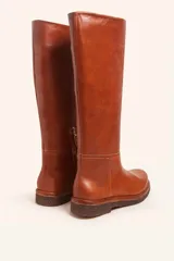 Bota de caña alta confeccionada en cuero vacuno suave, con diseño minimalista y suela de goma robusta. Presenta costuras visibles en la zona del empeine y un taco bajo cuadrado.