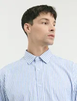 Camisa de manga larga con estampado de rayas verticales en azul y blanco, cuello clásico y bolsillo frontal.