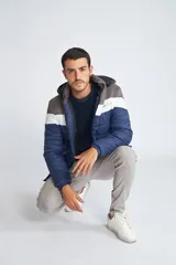 Campera inflada de abrigo para hombre, con capucha desmontable, cierre frontal completo, bolsillos con cierre y logo estampado. Diseño color block en azul, blanco y gris.