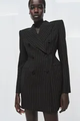 Blazer vestido de Zara con diseño de raya diplomática, cuello solapa con muesca, hombreras marcadas y cierre frontal cruzado con botones. Presenta una cintura entallada con volumen y falso bolsillo de vivo en el pecho.