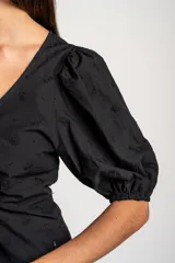 Blusa negra de algodón con diseño bordado sutil, escote en V y cordón ajustable fruncido en el centro del frente. Mangas cortas abullonadas.