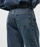 Pantalón de jean estilo balloon con cintura alta, corte amplio en cadera y piernas con ajuste leve en la botamanga. Presenta cierre frontal con botón, pasantes para cinturón y bolsillos funcionales.