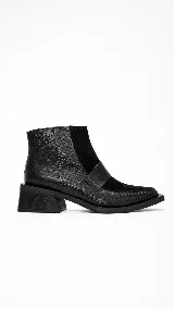 Botineta de cuero negro con diseño combinado de texturas reptil y gamuza. Presenta un taco cuadrado robusto y una puntera cuadrada con detalle de costura.