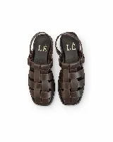 Sandalias de cuero marrón estilo romano, con tiras entrelazadas en el empeine, suela plana y tira ajustable en el talón.