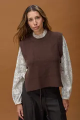Chaleco de punto color marrón, con cuello redondo y corte recto. Presenta un diseño minimalista con aberturas laterales amplias y detalle de tira con botón en los costados.