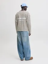 Remera de manga larga oversize con diseño a rayas horizontales en color marrón y crudo, cuello redondo en tono marrón contrastante y hombros caídos.