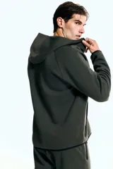 Campera deportiva de tejido funcional efecto neopreno color verde oscuro, con capucha, cierre frontal y bolsillos delanteros con cierre. Presenta mangas raglán y elástico fino en puños y bajo.