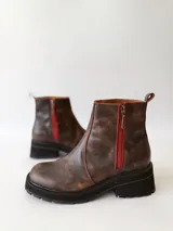 Botas cortas de cuero color chocolate, con elástico lateral, cierre interno con cremallera roja, pespuntes rojos y suela track.