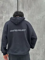 Canguro negro con capucha ajustable con cordones, bolsillo tipo canguro y estampado frontal con el texto "Crafted Project" y símbolos gráficos.