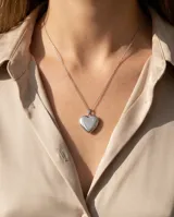Relicario de acero en forma de corazón con acabado pulido brillante, suspendido de una cadena de eslabones finos.