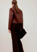 Chaqueta corta color bordó, de manga larga, con cuello camisero, bolsillos frontales con solapa y cierre de botones oscuros.