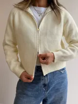 Cardigan tejido de textura suave con cierre frontal de doble vía, cuello alto y mangas largas. Presenta terminaciones en rib en puños y cintura, con un diseño versátil y moderno.