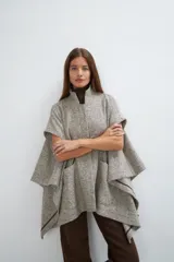 Capa de lana fina con cuello alto, cierre frontal con botones ocultos y bolsillos plaqué. Presenta aberturas laterales versátiles que permiten usarla como poncho o ruana, con terminaciones envivadas.