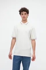 Remera polo manga corta color blanco, confeccionada en tela piqué de algodón lavado con textura extra suave. Cuenta con media cartera de botones, cuello y puños acanalados con diseño de líneas a contratono, y bordado sutil de la marca en el pecho. Calce clásico.