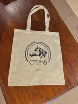 Bolso tipo tote bag de tela color beige con estampado frontal en negro de la S.C.C.C.U. de Criollos con la leyenda "Patrimonio Cultural de la República Oriental del Uruguay".