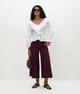 Pantalón tipo pantacourt de sastrería en color bordó, con pliegues delanteros, cintura con trabillas y cierre frontal. Presenta un corte amplio y sofisticado, e incluye un cinturón fino desmontable.