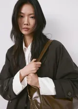 Chaqueta estilo gabardina larga en color gris oscuro, con doble botonadura frontal, solapas clásicas, bolsillos y trabillas ajustables en los puños.