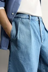 Bermuda de denim con corte relaxed fit, tiro medio y pierna recta. Presenta pliegues frontales dobles, bolsillos laterales y bolsillos traseros de doble vivo. Confeccionada en tejido rígido con efecto lavado, cierre frontal con cremallera y botón.