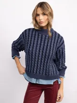 Sweater de punto con diseño de trenzas verticales, cuello alto y corte holgado. Presenta mangas largas con puños acanalados y un largo a la cadera.