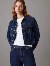 Campera de denim rígido color azul índigo oscuro, con corte cropped y ajuste auténtico de los 90. Presenta cuello en punta, bolsillos con solapa en el pecho y botones metálicos de la marca. Incluye una insignia con el logo de Calvin Klein en el bolsillo del pecho.