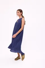 Vestido largo color beige, sin mangas, con escote redondo y abertura en forma de gota en el pecho. Tiene corte holgado y ruedo con volantes.