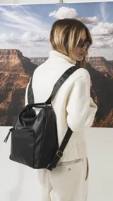 Cartera mochila de cuero sintético color tostado, con diseño versátil que permite usarla al hombro o como mochila. Presenta un bolsillo frontal con cierre, apertura superior y correas ajustables.
