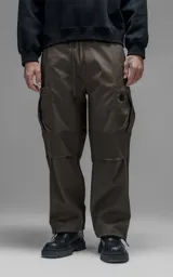 Pantalón cargo de corte regular confeccionado en textil técnico pesado color chocolate. Presenta cintura elástica con cordón de ajuste, dos bolsillos laterales en la cintura y dos bolsillos cargo de gran tamaño. Incluye elásticos con tancas en los tobillos para regular la apertura de la pierna.