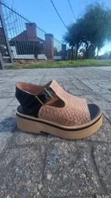 Zueco abierto de cuero con plataforma, capellada ancha con textura símil serpiente en tono tostado y tira trasera negra con hebilla metálica.