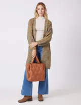 Cartera de eco cuero color marrón, con diseño capitoneado en rombos de gran relieve. Cuenta con un compartimento principal con cierre, amplios bolsillos laterales con botones imantados, asa de mano fija y correa larga regulable y removible. El forro interno es textil a tono con compartimentos organizadores.