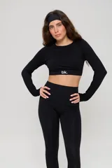 Conjunto deportivo de tres piezas en color negro, compuesto por un top de manga larga con cuello redondo y logo estampado, un top de bretel ancho y una calza chupín de tiro alto. El diseño presenta detalles de tejido con textura en zonas estratégicas.