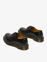 Zapato de cuero negro Dr. Martens modelo 1461, con tres ojales, costuras amarillas y suela con cámara de aire resistente al aceite y a la abrasión.
