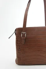 Cartera de hombro estructurada color negro, confeccionada en 100% cuero vacuno con textura en relieve tipo reptil. Cuenta con asas largas ajustables mediante hebillas metálicas plateadas, cierre superior y el logo de la marca grabado en la parte frontal.