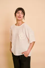 Blusa holgada color beige con mangas cortas y cuello redondo. Presenta apliques bordados con detalles de perlas y lentejuelas en el frente.