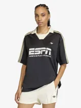 Camiseta de estilo futbolístico con cuello polo, manga corta y corte holgado. Presenta un diseño en color negro con detalles en blanco y amarillo en las mangas, y el logo de la marca junto a un estampado gráfico frontal.