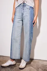 Jean de tiro medio, corte recto y largo cropped, confeccionado en denim de algodón con elastano. Presenta un efecto de lavado bicolor o combinado, con paneles de diferente tono de azul claro, y costuras verticales marcadas en el frente. El ruedo es deshilachado.