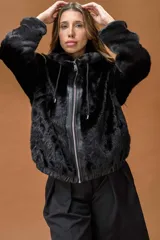 Campera tipo bomber de piel sintética negra con textura aterciopelada. Presenta capucha, cierre frontal con cremallera metálica y detalles en cuero sintético en la zona del cierre y los puños.