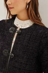 Saco corto de textura tweed en color azul oscuro con destellos metalizados. Presenta cierre frontal mediante tres trabas de cuero sintético con botones tipo toggle, cuello redondo y mangas largas.