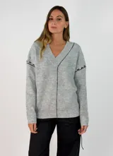 Sweater de punto gris con cuello en V, manga larga y detalles de costuras decorativas en color negro a lo largo del centro y en las mangas.